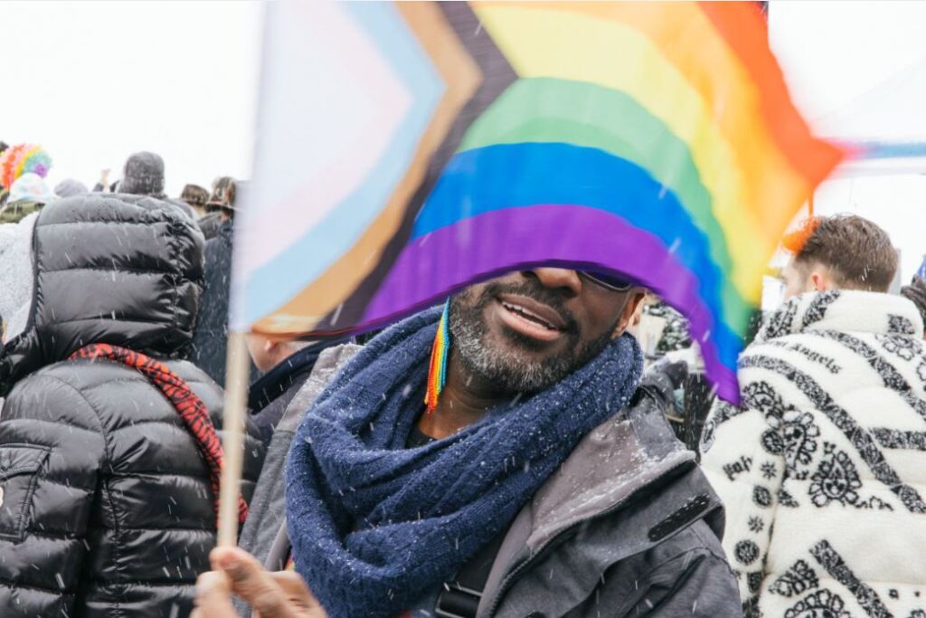 Man sports a gay pride flag in a snowy and festive image during Gay Ski week in Aspen Colorado.