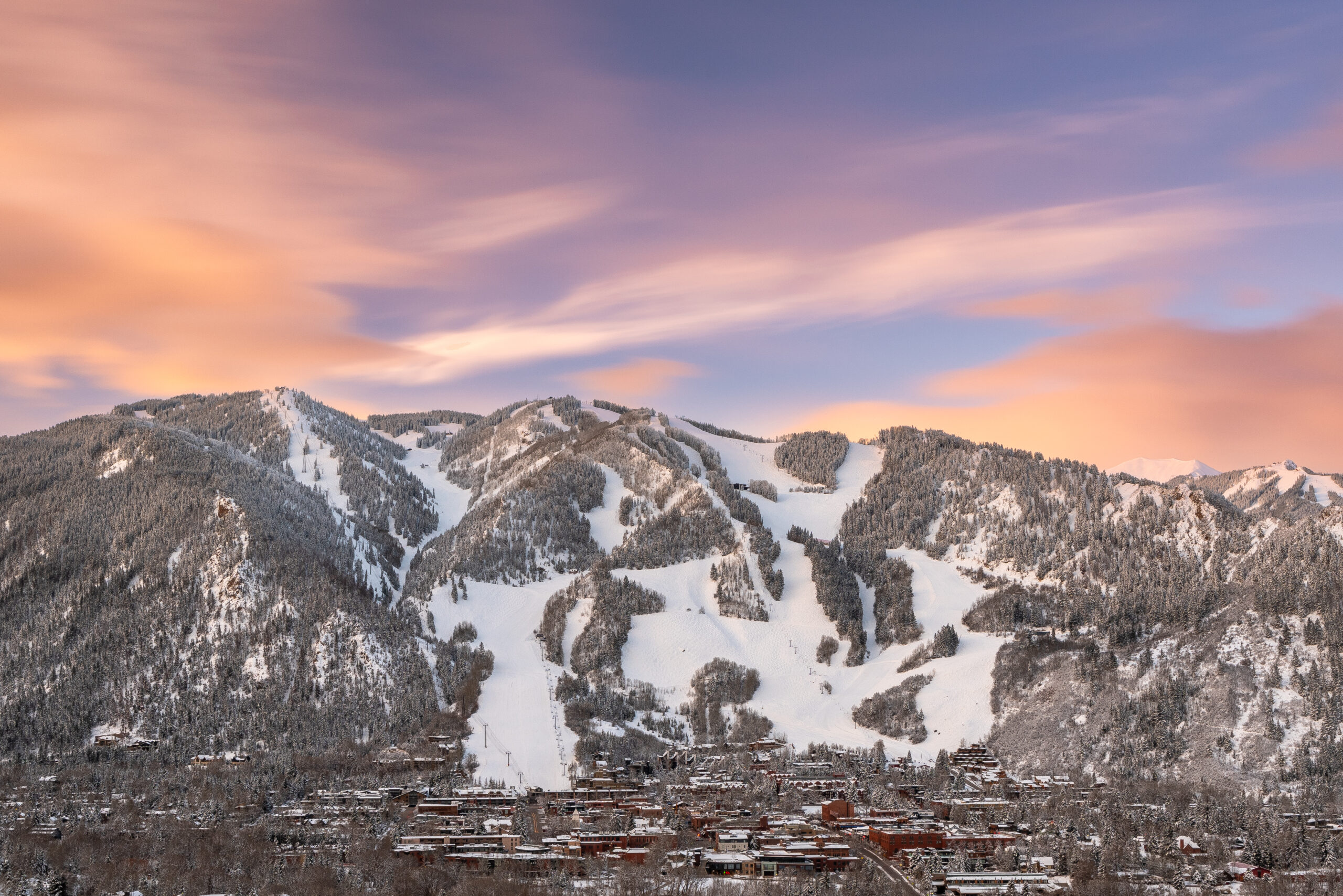 Aspen Mountain, at sunset, snowy runs below the pink and blue sky, with the town of aspen nestled underneath