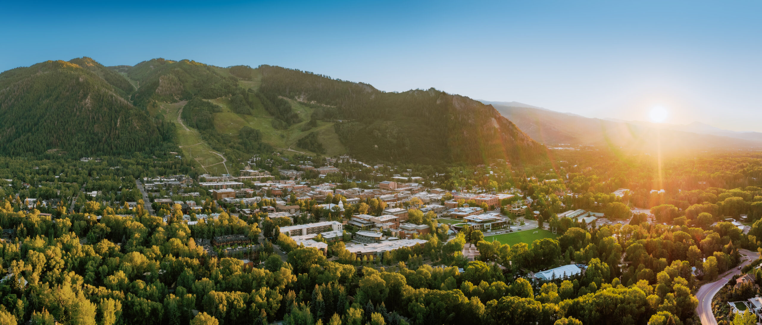 Sun rises over the mountains of Aspen, casting a golden glow over the town of aspen, green trees cover the slopes of aspen mountain