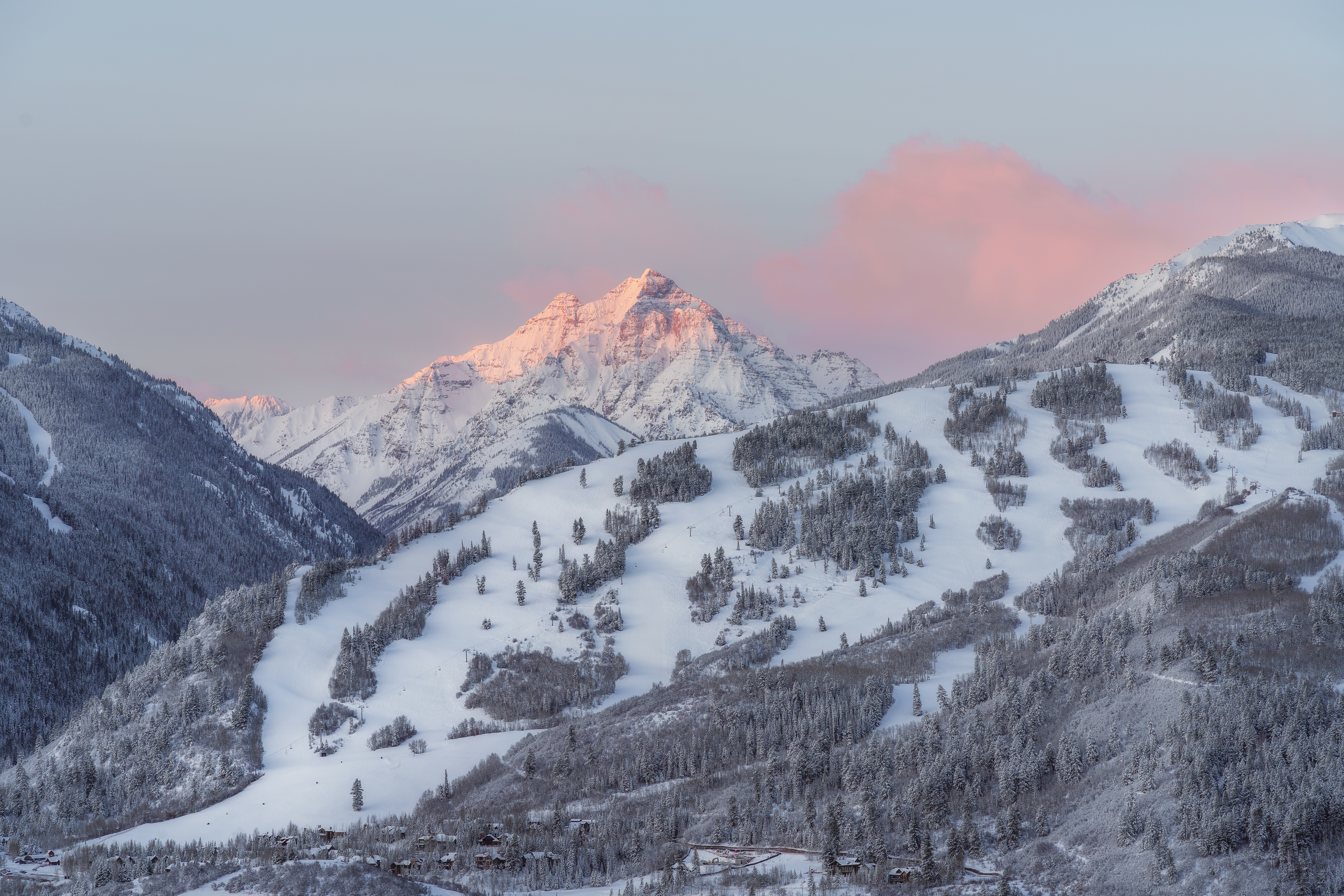 Pink clouds over white, snow capped mountains, white snowy ski runs are still in the shadow on the sun hasn't risen of buttermilk mountain yet