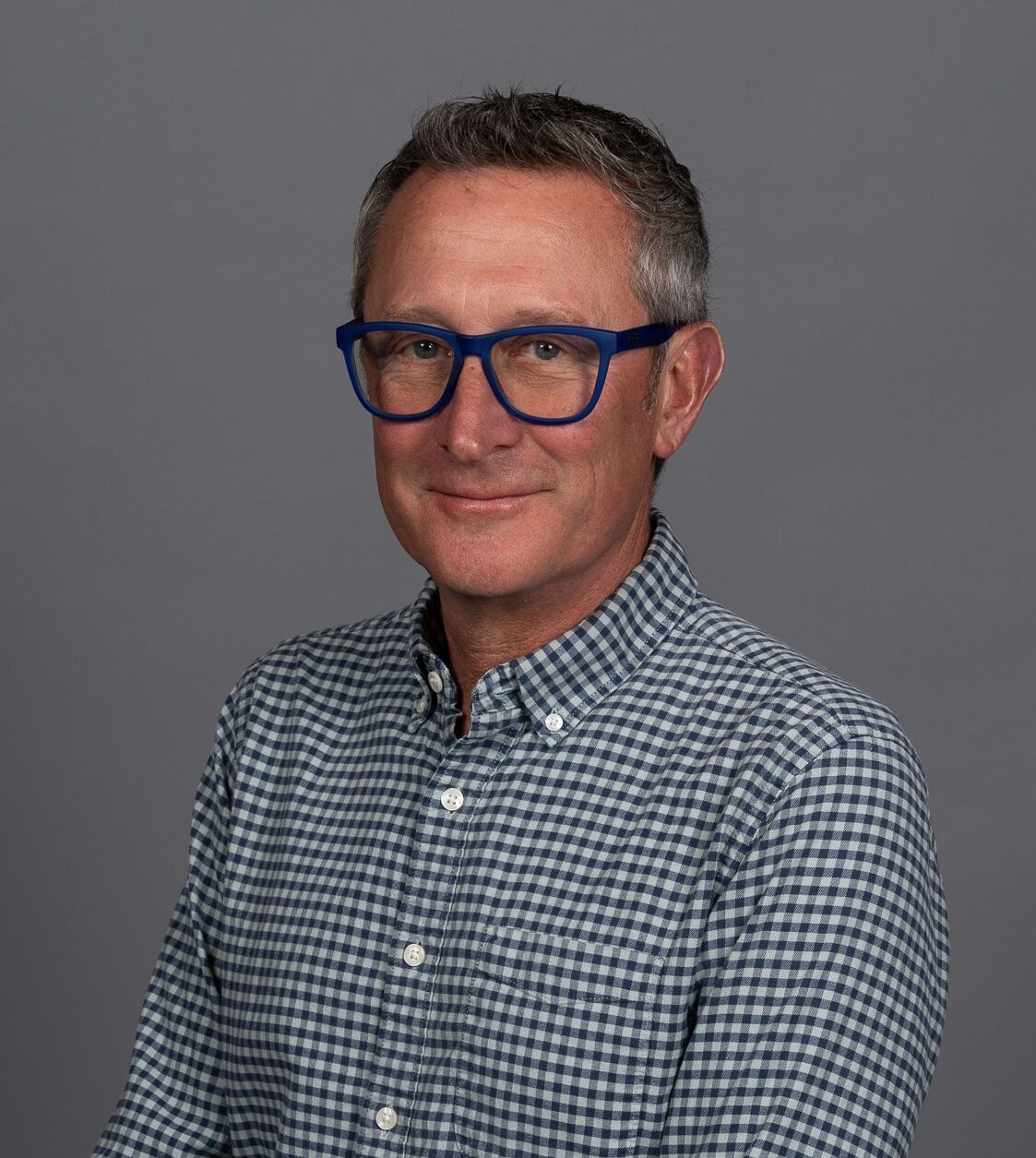 Headshot of Chris Miller, Senior VP of sustainability. He is a man in a blue and white checkered shirt and blue, thick rimmed glasses
